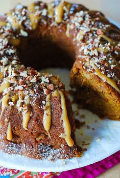 a bundt cake with nuts and caramel drizzled on top sits on a plate