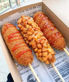 two chicken skewers with ketchup on them in a cardboard box next to a paper wrapper