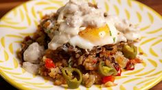 a yellow and white plate topped with rice covered in an egg, peppers and onions