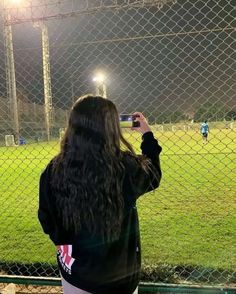 a woman taking a photo with her cell phone in front of a soccer field at night