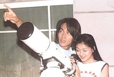 a man and woman standing next to each other in front of a telescope