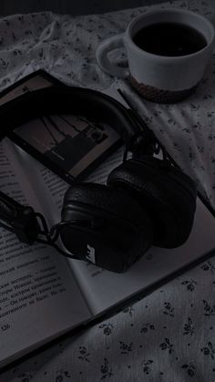 an open book with headphones on top of it next to a cup of coffee