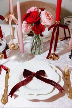 the table is set with red and pink flowers in vases, silverware, and candles