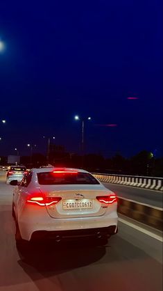 the back end of a white car driving down a highway at night with lights on