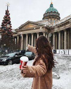 a woman holding a red and white cup in front of a building on a snowy day