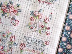 two cross stitched quilts with flowers and hearts on them, one has the word love written in cursive writing