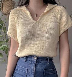 a woman wearing a yellow knitted sweater and blue denim skirt standing in front of a potted plant