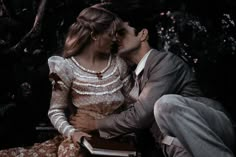 a man and woman sitting next to each other in front of some trees with flowers