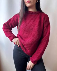 a woman is wearing a red sweater and black pants with her hands on her hips