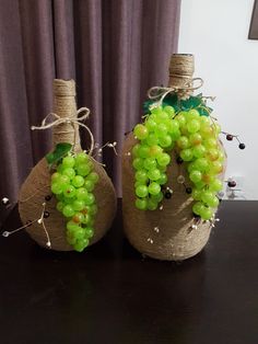 two wine bottles decorated with green grapes and twine of twine on a table