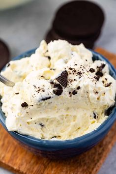 a blue bowl filled with ice cream and oreo cookies on top of a wooden cutting board