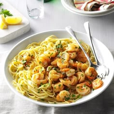 a white bowl filled with pasta and shrimp on top of a table next to two plates of food