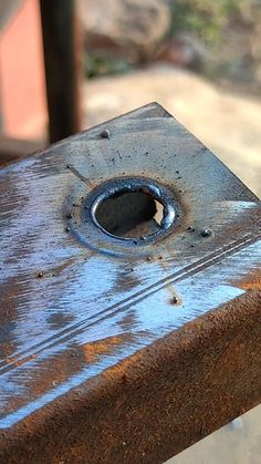 an old rusted metal object with holes in the center sitting on a wooden bench