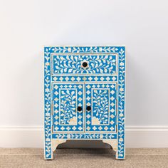 an ornate blue and white cabinet with drawers on the bottom, against a plain wall