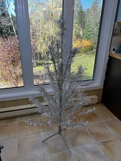 a silver christmas tree sitting in front of a window on top of a tile floor