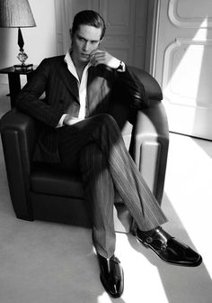 a man sitting in a chair with his legs crossed and wearing a suit, tie and shoes