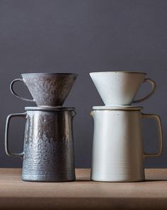 three coffee cups sitting on top of a table next to each other, one white and one gray