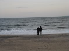 two people standing on the beach looking out at the ocean