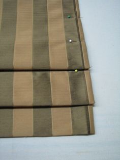 three pieces of fabric sitting on top of a white tablecloth covered in green and brown stripes