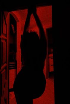 a woman is silhouetted against a red light in a dark room with an open door