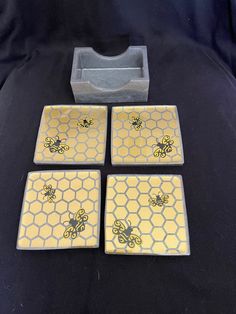 four coasters with bees on them sitting next to a cup and tray in the shape of a honeycomb