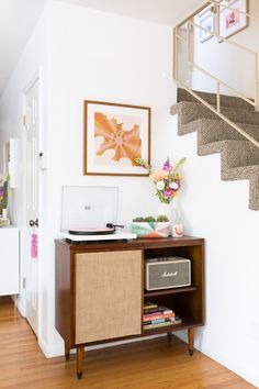 a laptop computer sitting on top of a wooden cabinet next to a stair case in a living room