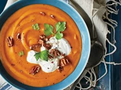 a blue bowl filled with carrot soup topped with sour cream and chopped pecans, garnished with parsley