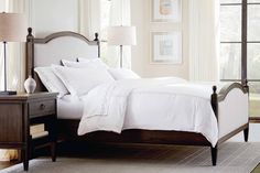 a bed with white sheets and pillows in a bedroom next to two lamps on either side of the bed