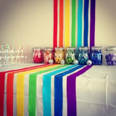 candy jars lined up on top of a table with rainbow colored streamers in them