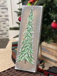 a christmas tree painted on a canvas next to a small train track with ornaments in the background