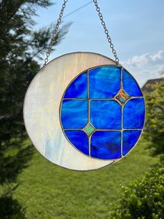 a blue and white stained glass sun catcher hanging from a chain in front of some trees