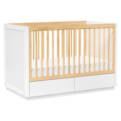 a white crib with wood trim and drawers on the bottom shelf, in front of a white background