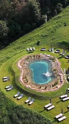 an aerial view of a pool in the middle of a lush green field with chaise lounges around it