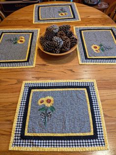 four place mats with sunflowers and pine cones in them on a wooden table