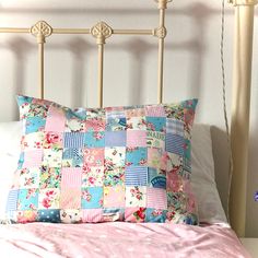 a bed with a pink comforter and pillows on it's headboard, in front of a white wall