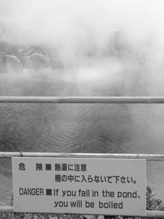 a sign that is on the side of a fence near some water with steam rising from it