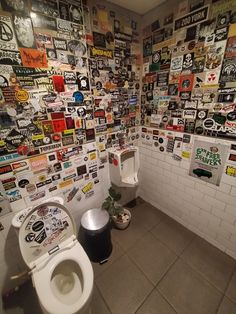 two toilets in a bathroom with many stickers on the wall