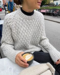 a woman sitting at a table with a cup of coffee in her hand and looking off into the distance