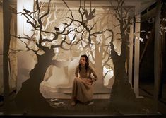 a woman sitting on a bench in front of a wall with trees painted on it