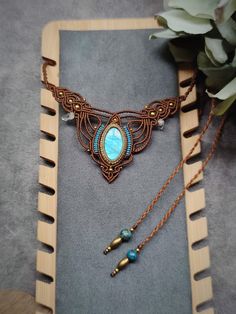 a necklace with a blue stone and some gold beads on it next to a plant