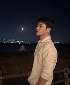 a man standing in front of a fence looking at the sky with a full moon behind him