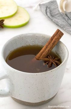 an apple cider with cinnamon stick in it next to sliced apples on a table