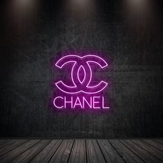 a chanel neon sign is lit up on the wall in front of a wooden floor