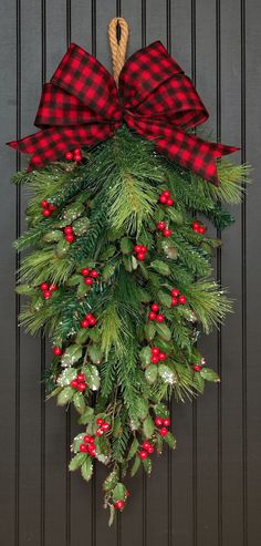 a christmas wreath hanging on the side of a door with red and black plaid bow