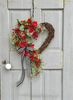 a heart shaped wreath with red flowers hanging on a door