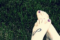 a woman's feet with purple nail polish and an i tattoo on her left foot