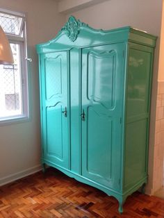 a green armoire sitting on top of a hard wood floor next to a window