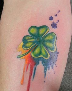 a tattoo with a four leaf clover painted on it's arm and watercolor splatters