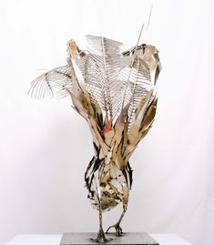 a sculpture made out of metal leaves on top of a white surface with a white wall in the background