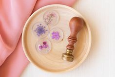 a wooden tray with buttons and a rubber stamper on it next to pink fabric